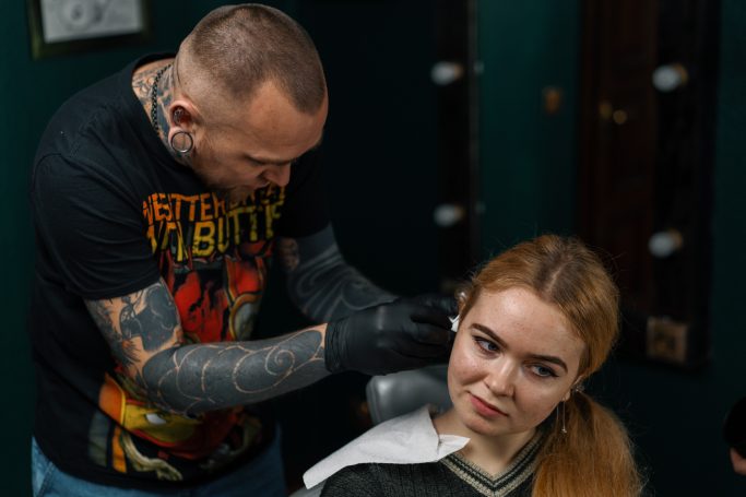 Piercer macht ein Piercing am Ohr